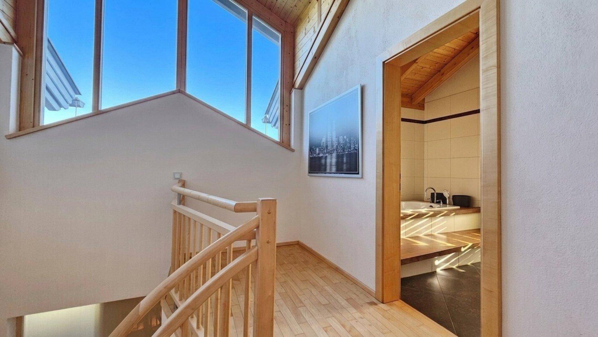 Oberer Flur mit Holzboden und Dachschräge, der zu einem Badezimmer mit Badewanne führt.