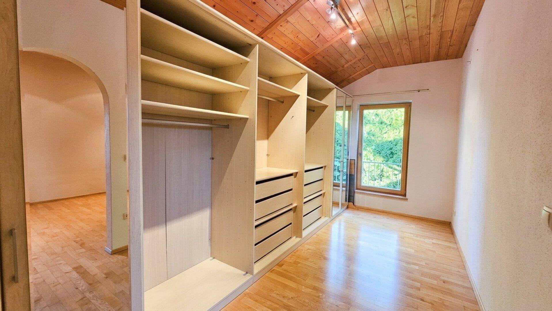 Geräumiger begehbarer Kleiderschrank mit maßgefertigten Regalen und Holzboden unter einer Holzdecke.