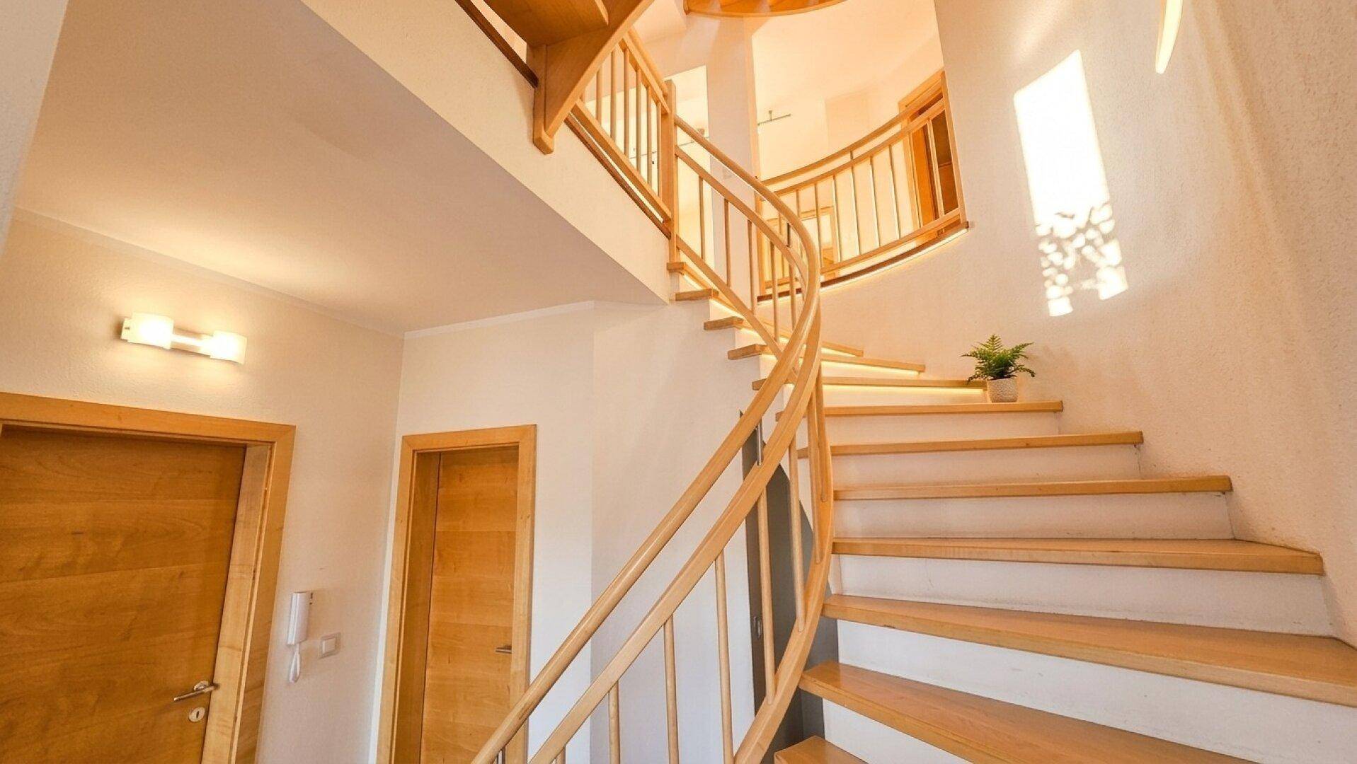 Heller Treppenaufgang mit geschwungener Holztreppe, die die verschiedenen Ebenen des Hauses verbindet.
