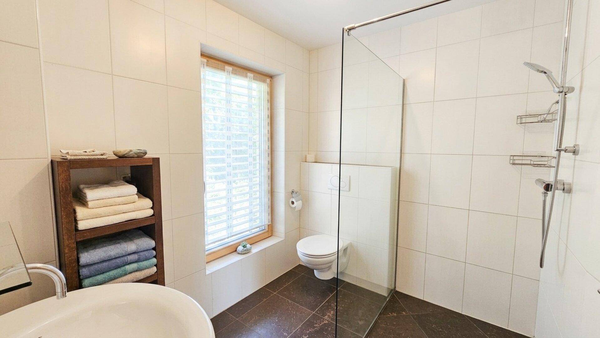Modernes Badezimmer mit ebenerdiger Dusche, wandhängendem WC und einem Fenster für Tageslicht.