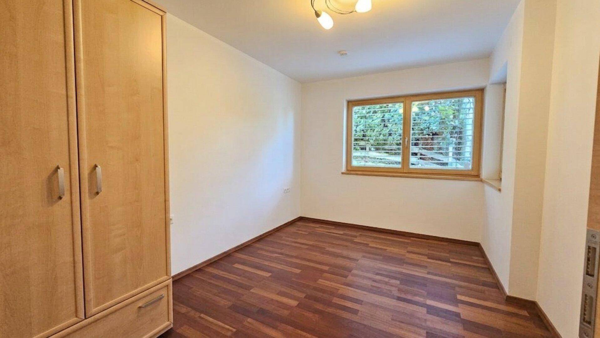Gemütliches Schlafzimmer mit Parkettboden, einem Fenster mit Jalousien und einem praktischen Holzschrank.