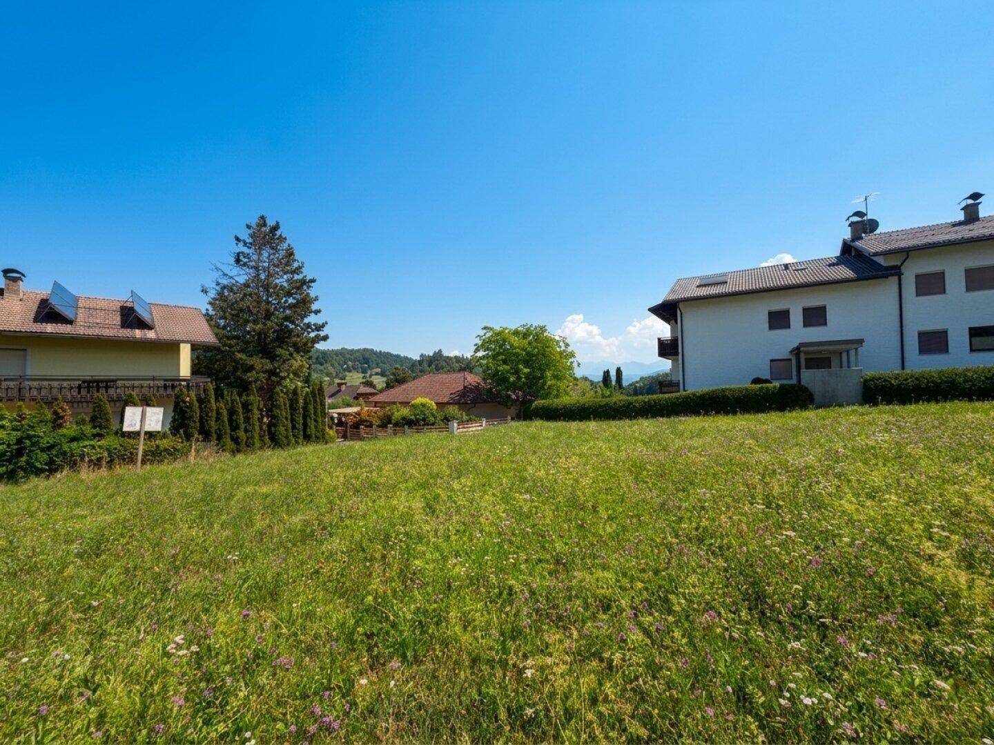 Weitläufiges grünes Grundstück mit Blick auf umliegende Häuser und die hügelige Landschaft unter blauem Himmel.