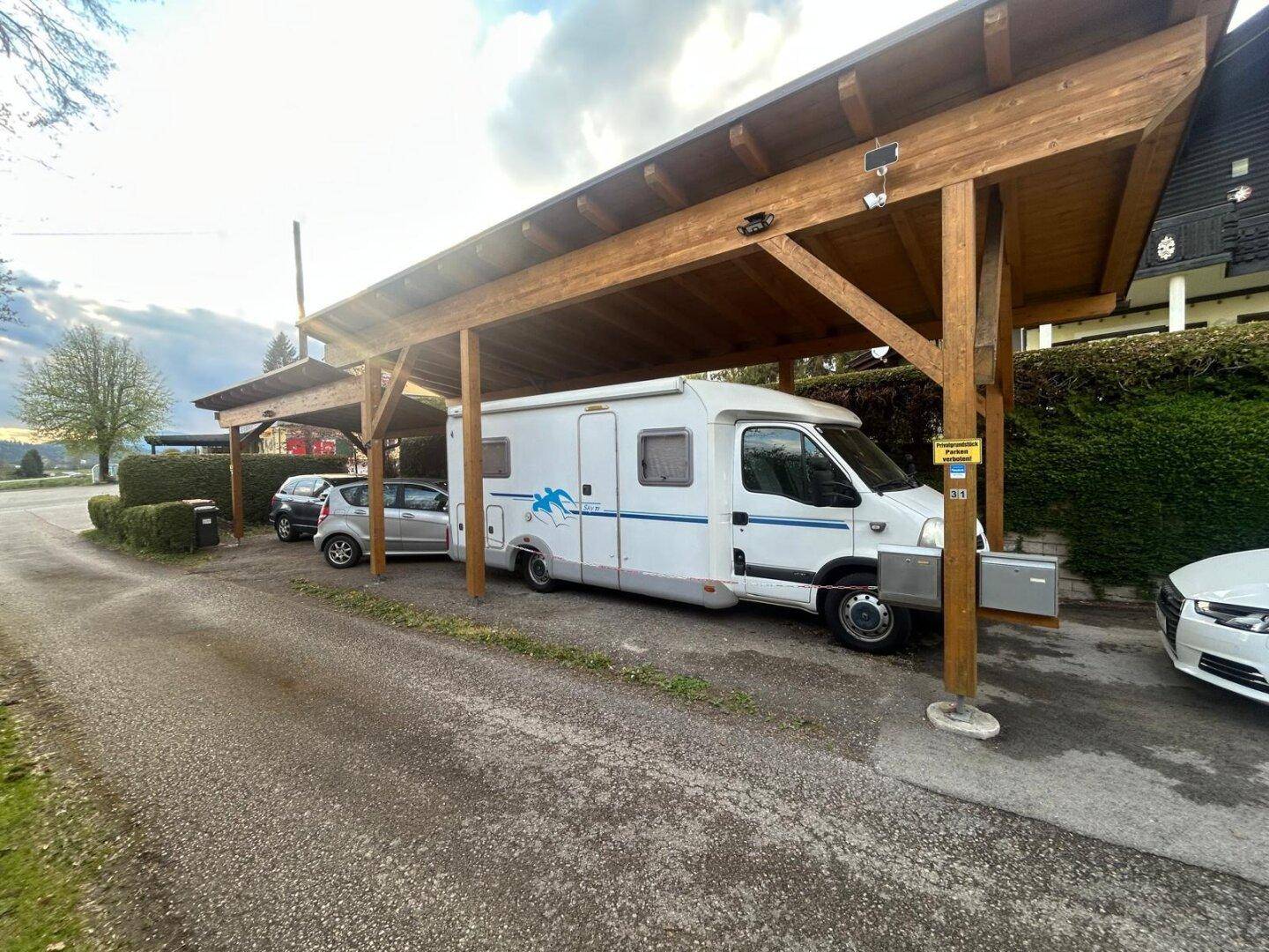 Überdachter Carport aus Holz bietet Schutz für Fahrzeuge, inklusive Wohnmobil und PKW.