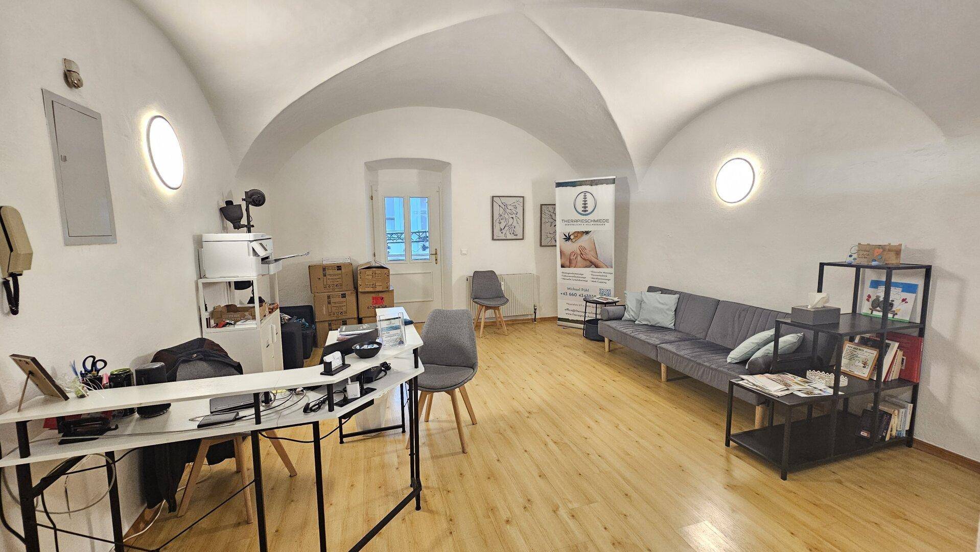 Empfangsbereich mit gewölbter Decke, Holzboden und moderner Einrichtung für Patienten oder Kunden.
