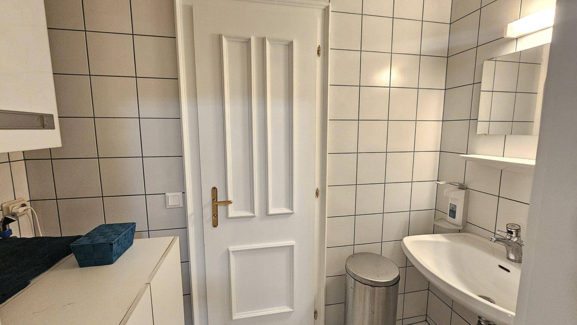 Badezimmer mit weißen Fliesen, einem Waschbecken und einer schlichten Tür.