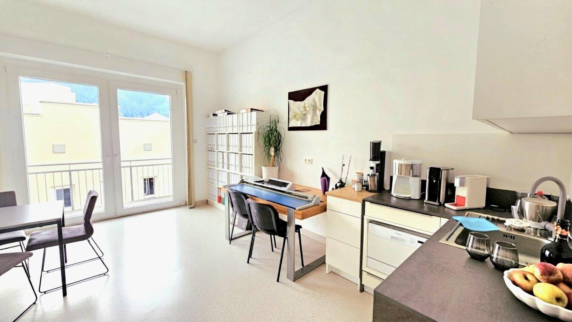 Offener Bereich mit kleiner Küche, Essplatz und Zugang zu einem Balkon.