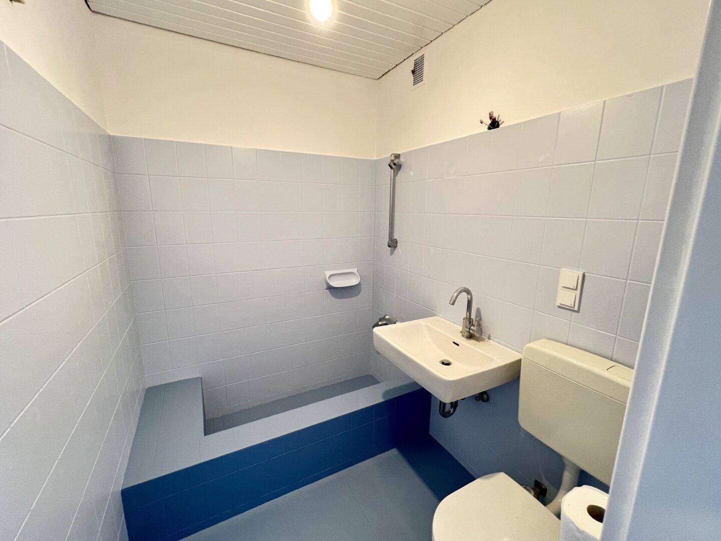 Badezimmer mit hellblauen Fliesen, WC, Waschbecken und Duschbereich.