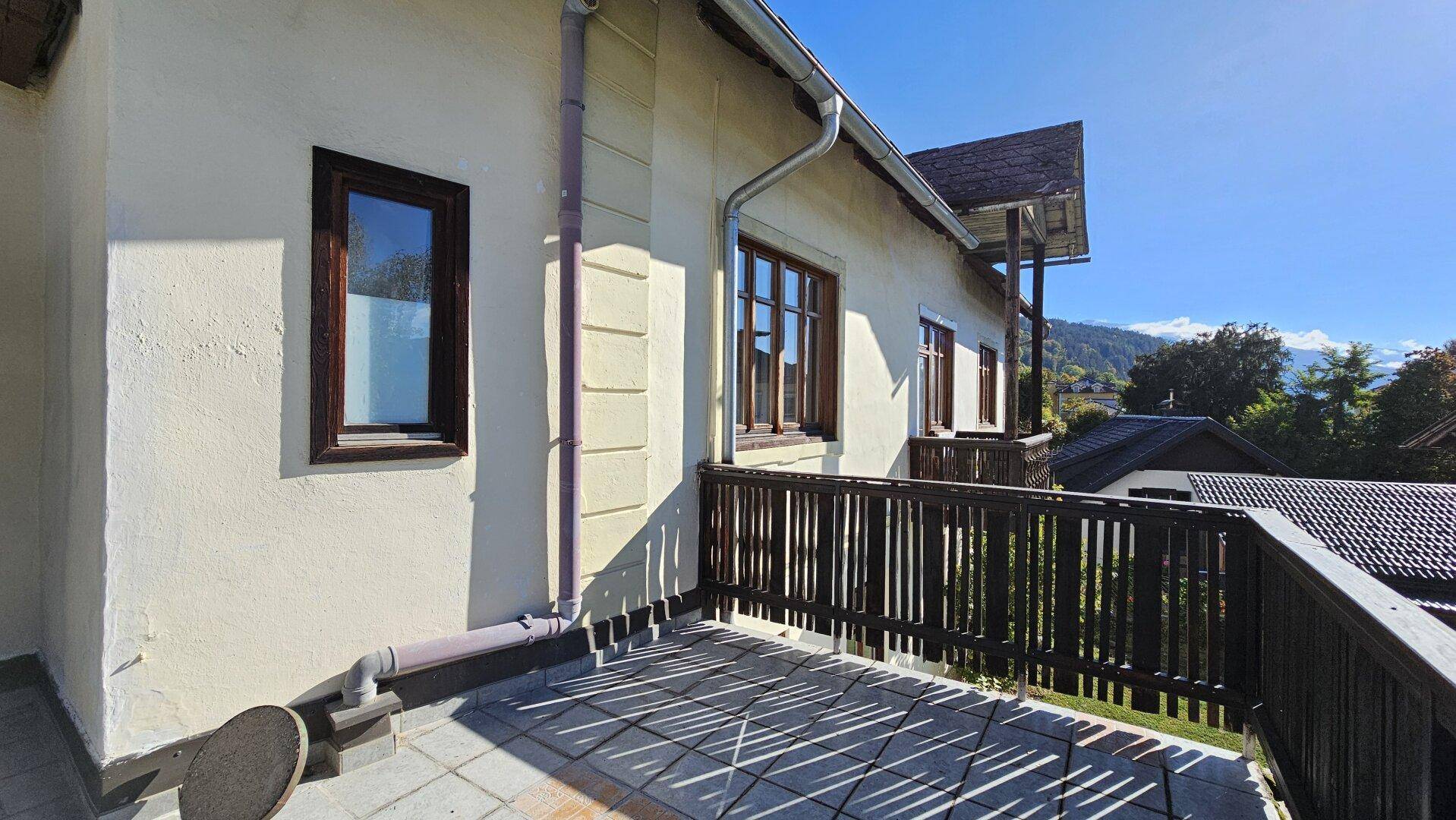Balkon mit Holzgeländer und Fliesenboden, angrenzend an die helle Fassade des Gebäudes.