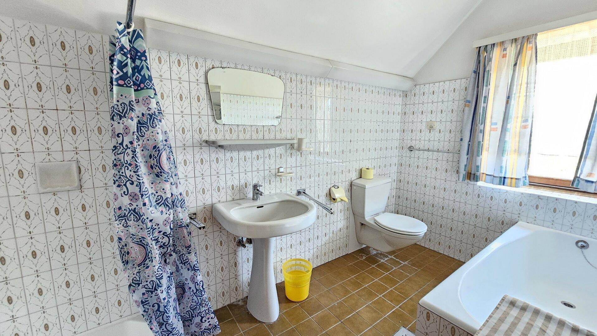 Helles Badezimmer mit Badewanne, WC, Standwaschbecken und gemusterten Fliesen.