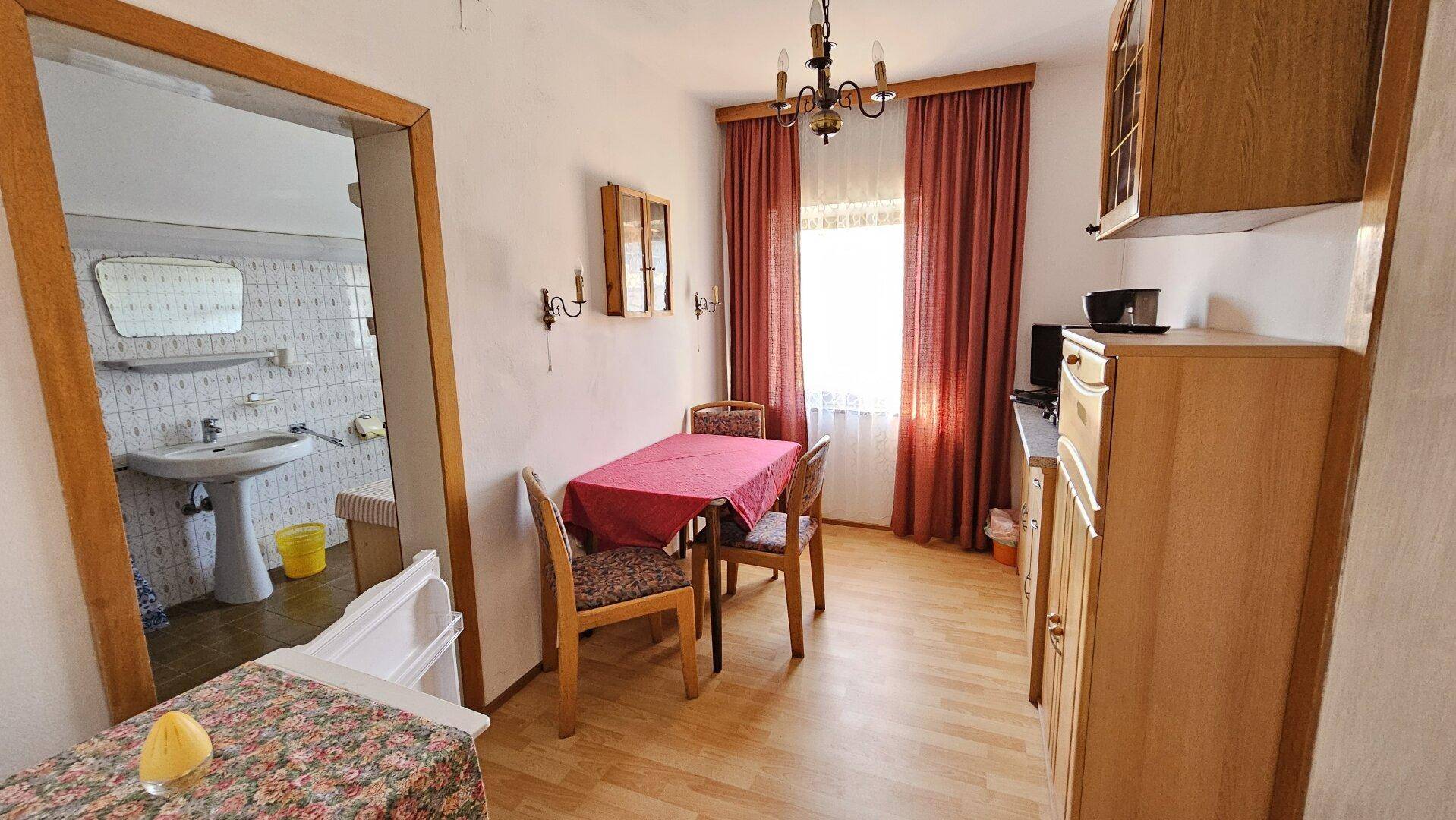 Essbereich mit Holztisch und Stühlen, angrenzend an ein Badezimmer.