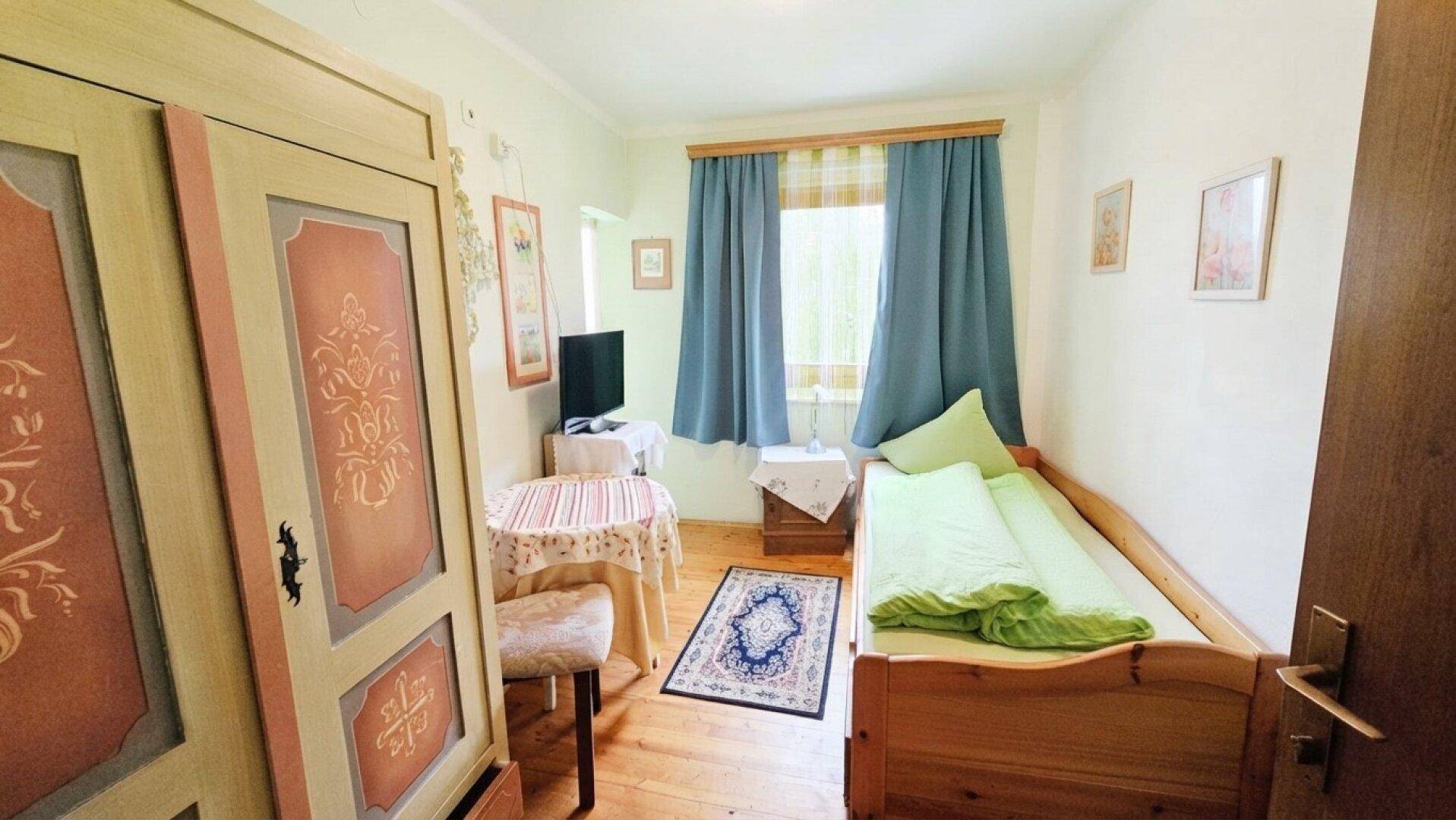 Kleines Schlafzimmer mit Einzelbett, Beistelltisch und einem verzierten Kleiderschrank.