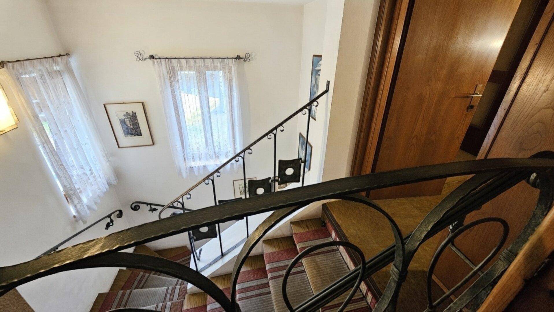 Geschwungene Treppe mit gemustertem Teppich und kunstvollem schmiedeeisernem Geländer führt in die oberen Stockwerke.