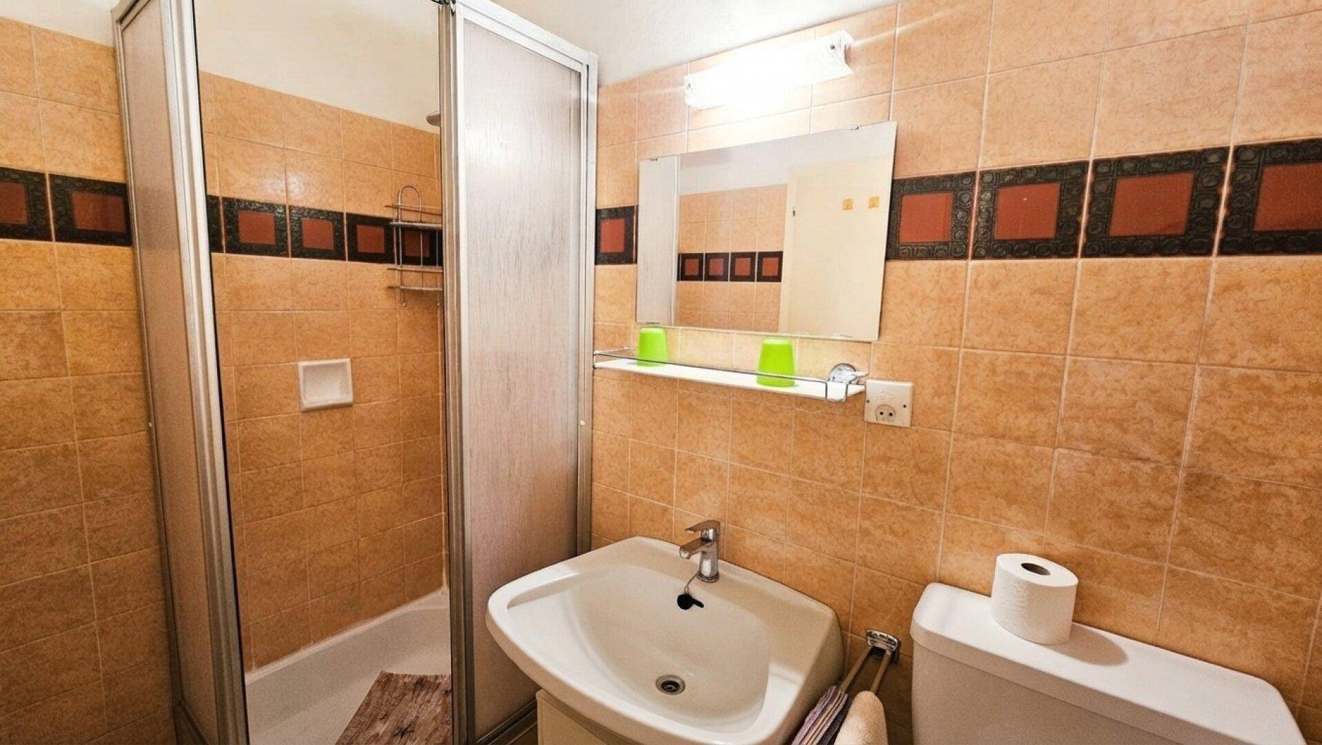 Funktionales Badezimmer mit beigefarbenen Fliesen, Duschkabine und einem einzelnen Waschbecken.