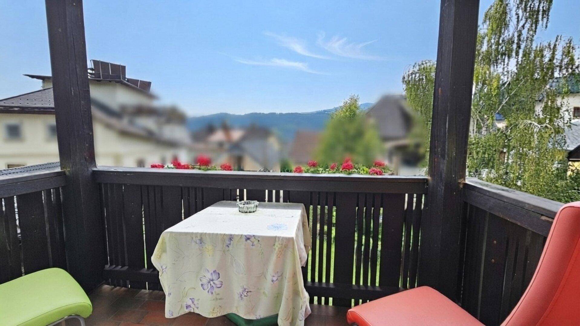 Kleiner Balkon mit Tisch und Stühlen, geschmückt mit Blumen und Bergblick.
