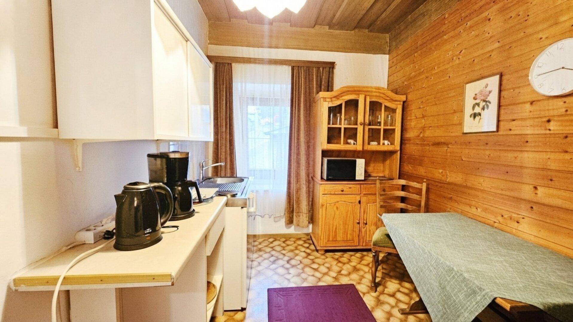 Rustikale Küchenzeile mit Holzvertäfelung, weißen Schränken und einem kleinen Essbereich.