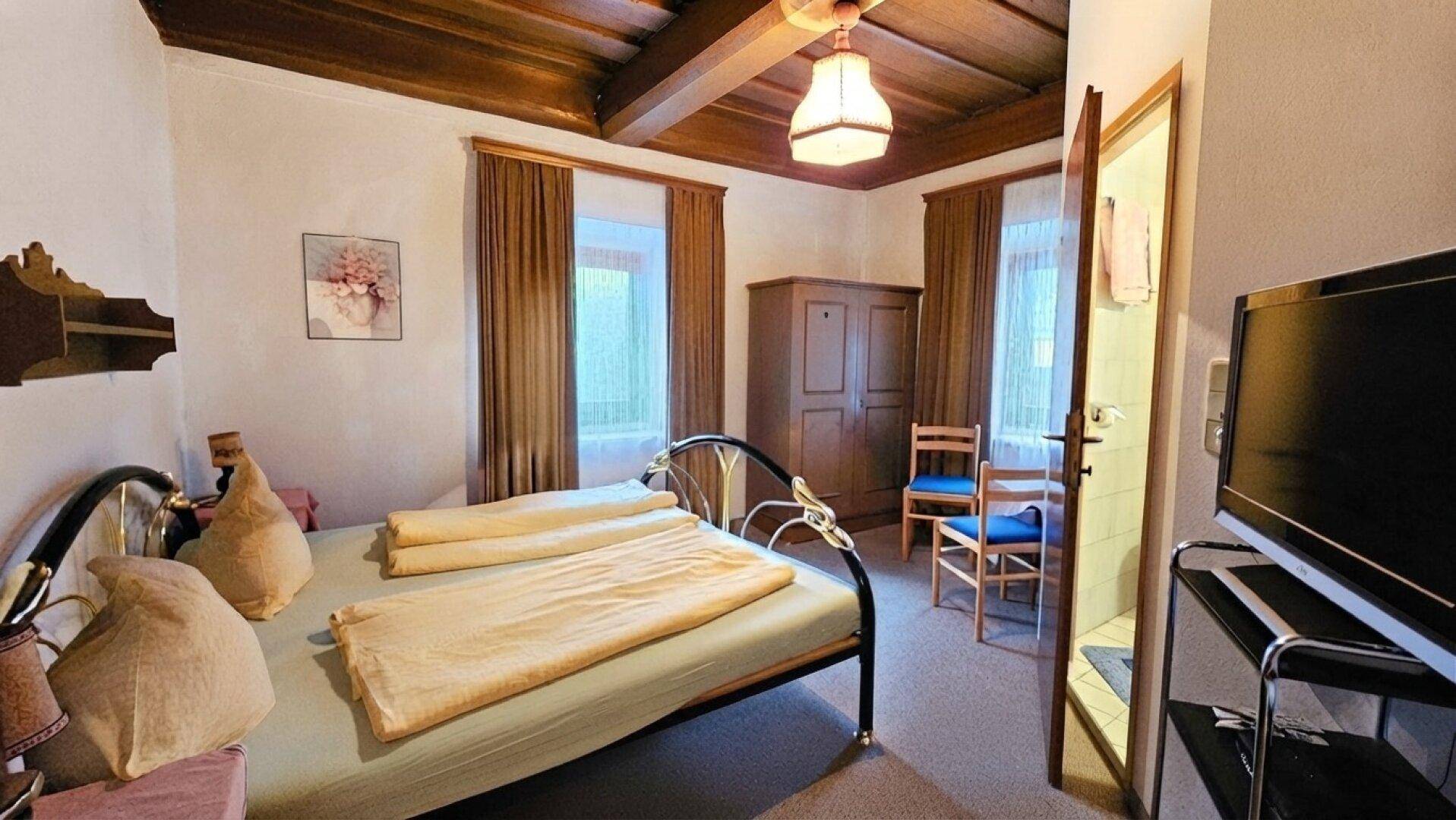Gemütliches Schlafzimmer mit Doppelbett, Holzbalkendecke und traditionellen Möbeln, ausgestattet mit Teppichboden.