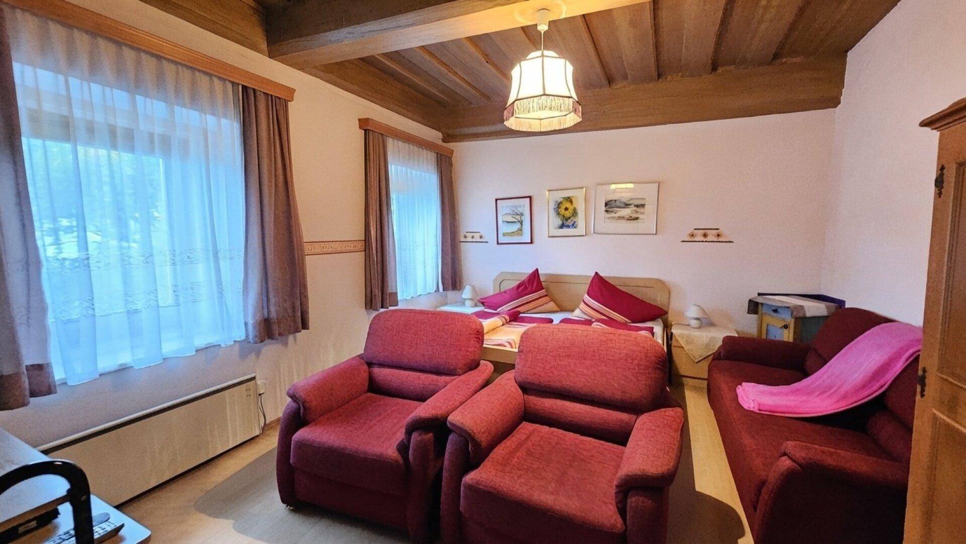 Schlafzimmer mit Doppelbett, zwei roten Sesseln und Holzbalkendecke, bietet eine gemütliche Atmosphäre.