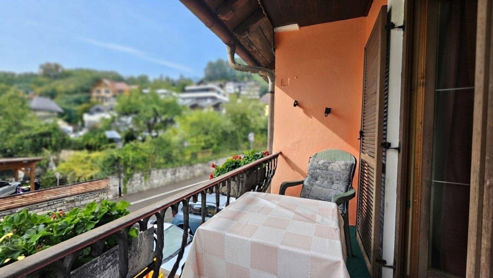 Kleiner Balkon mit Tisch und Stuhl, bietet einen Blick auf die grüne Umgebung und die Straße.