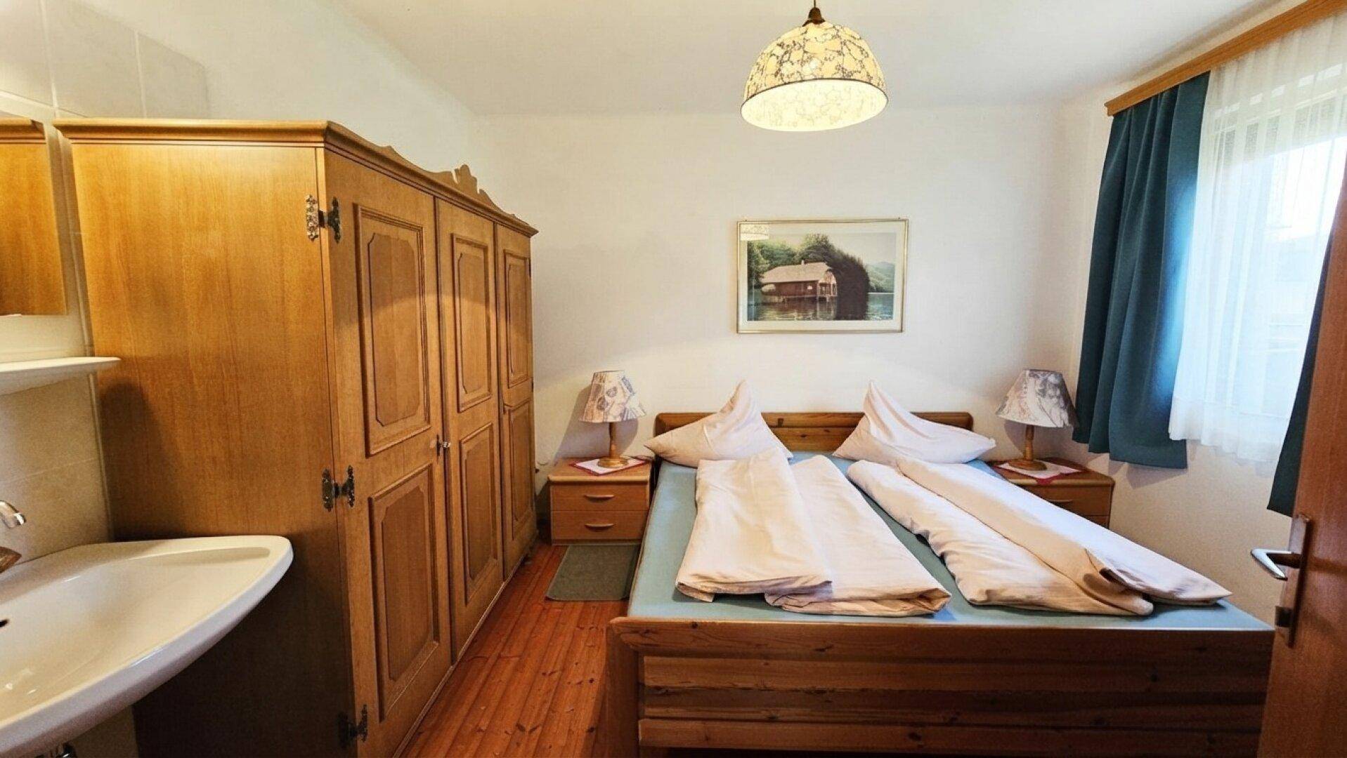 Gemütliches Schlafzimmer mit Doppelbett, großem Holzschrank und einem Waschbecken im Raum.