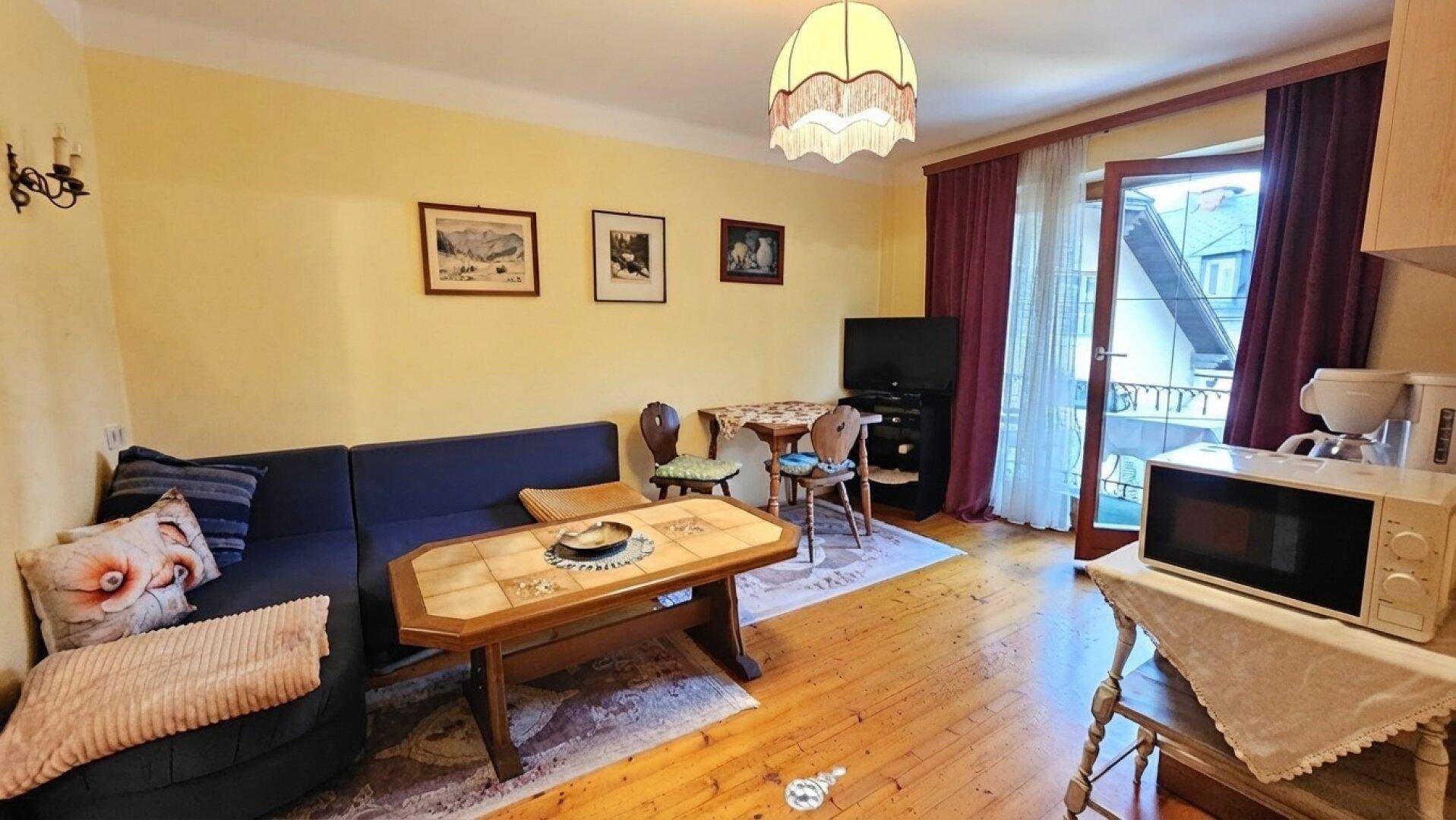 Wohnzimmer mit Sofa, Couchtisch und Zugang zum Balkon, ausgestattet mit Holzboden und Teppich.