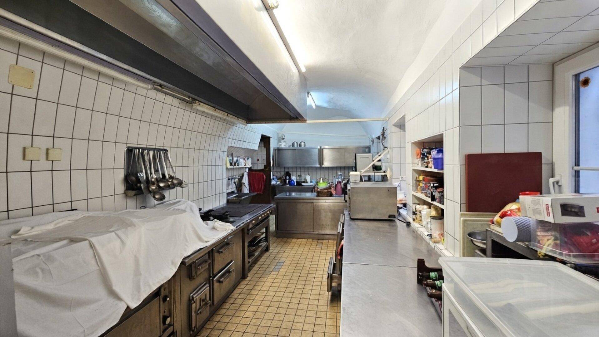 Professionelle Großküche mit Edelstahlgeräten, weißen Fliesen und industrieller Ausstattung für den Gastronomiebetrieb.
