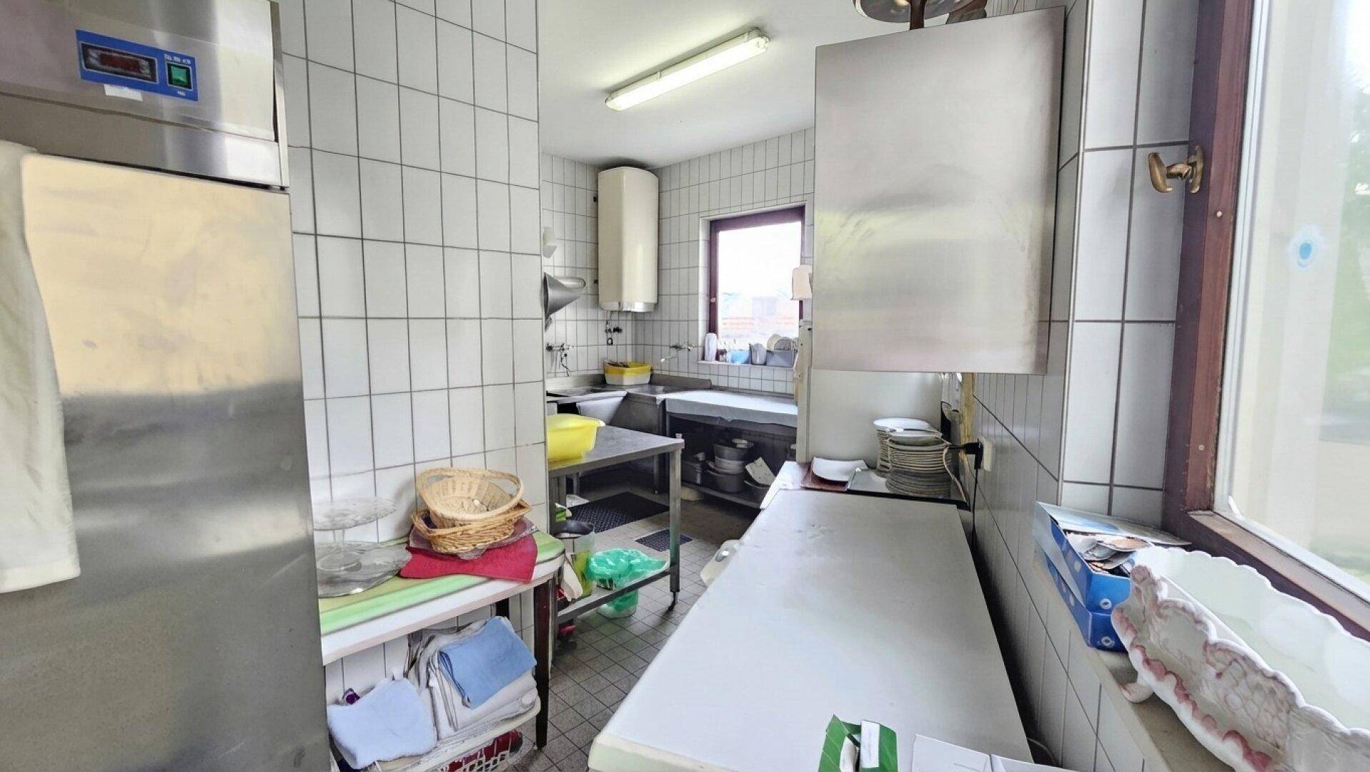 Helle Gewerbeküche mit Edelstahlflächen, Fliesenwänden und einem Fenster für natürliche Belüftung und Licht.