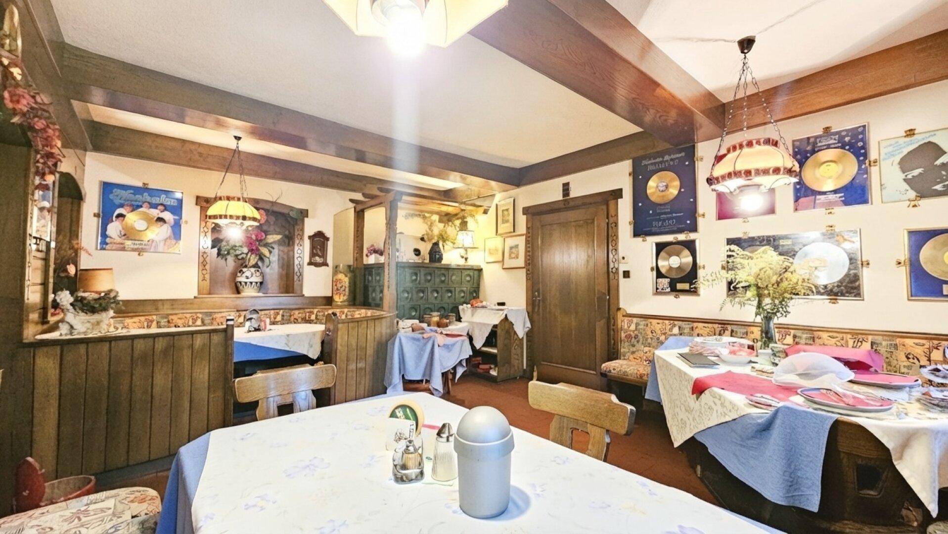 Gemütlicher traditioneller Essbereich mit Holztäfelung, karierten Tischdecken und dekorativen Elementen an den Wänden.
