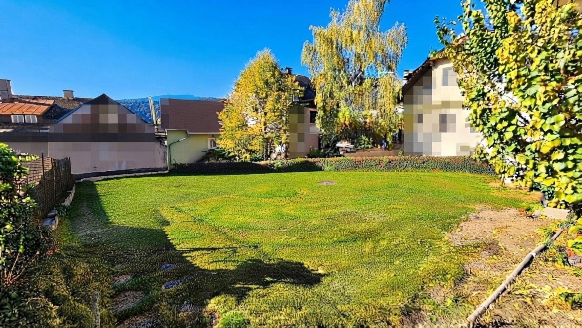 Weitläufiger Rasenbereich mit Bäumen und umliegenden Gebäuden unter blauem Himmel.