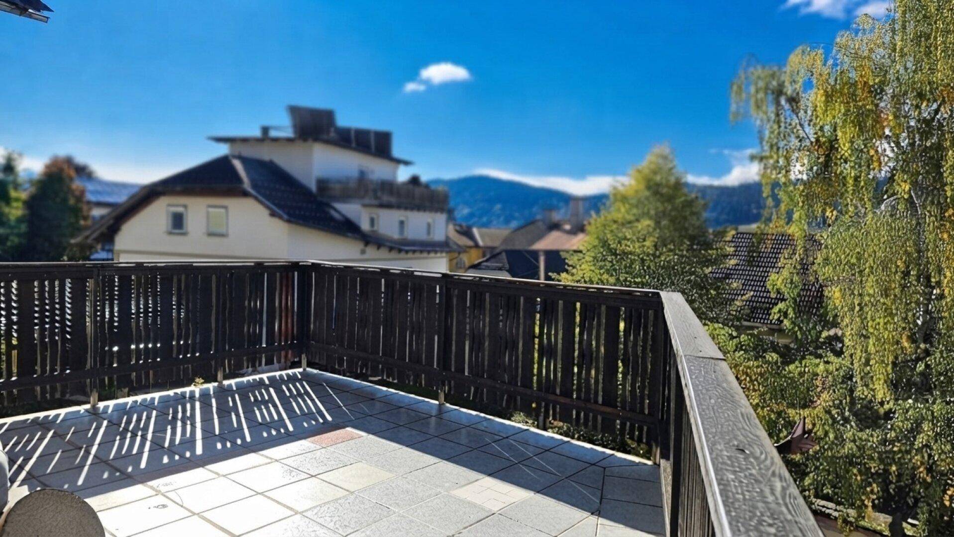Geräumiger Balkon mit Fliesenboden und Holzgeländer, bietet einen weiten Blick auf die Berge.