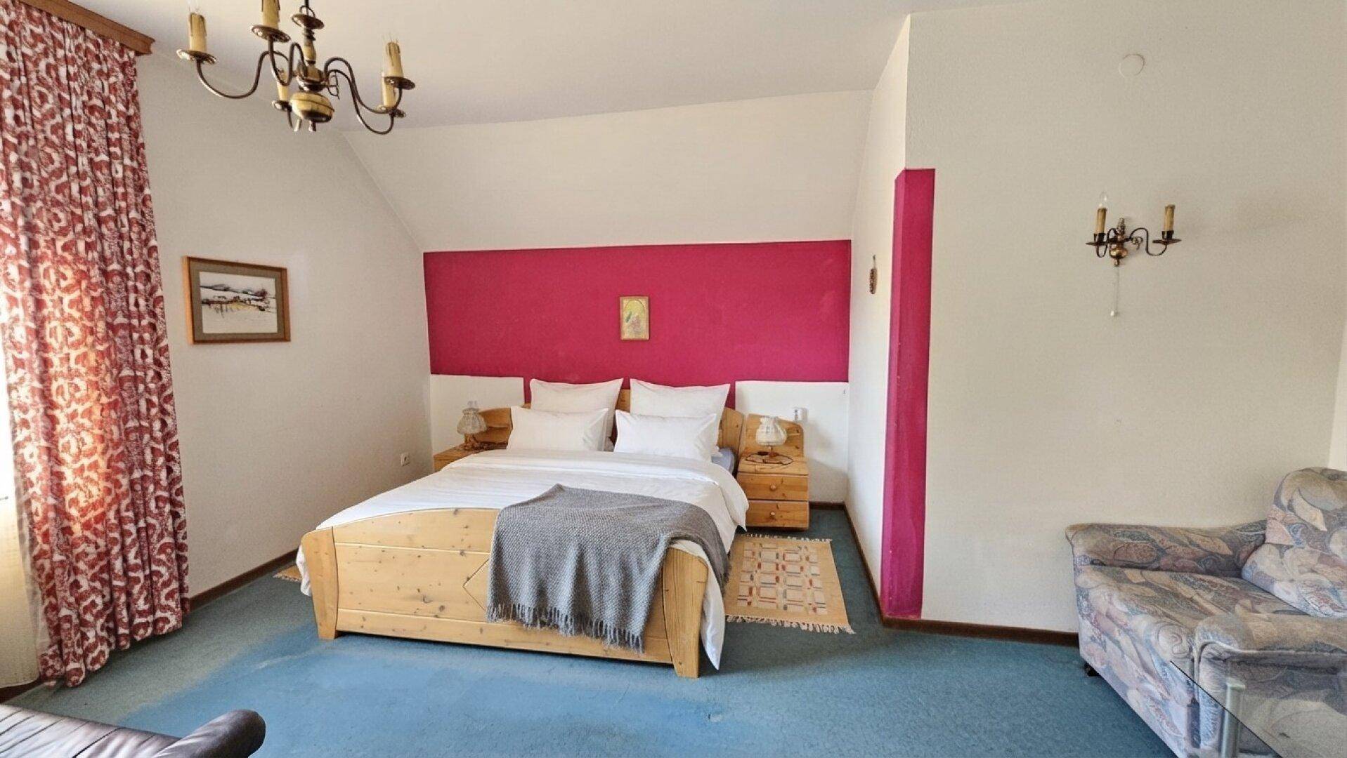 Helles Schlafzimmer mit Doppelbett, farbiger Akzentwand und blauem Teppichboden.