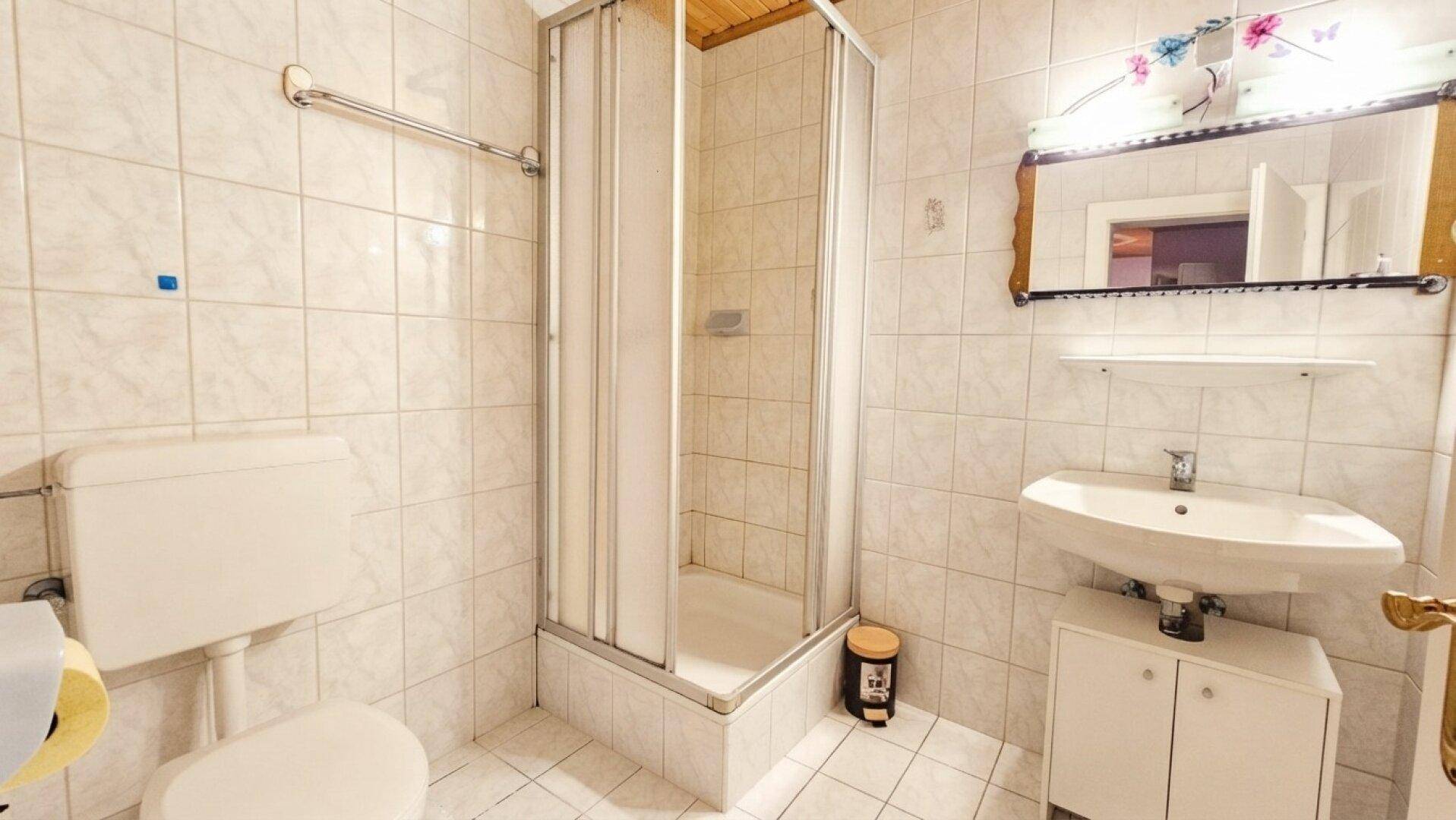Funktionales Badezimmer mit Duschkabine, WC und Waschbecken mit Unterschrank.