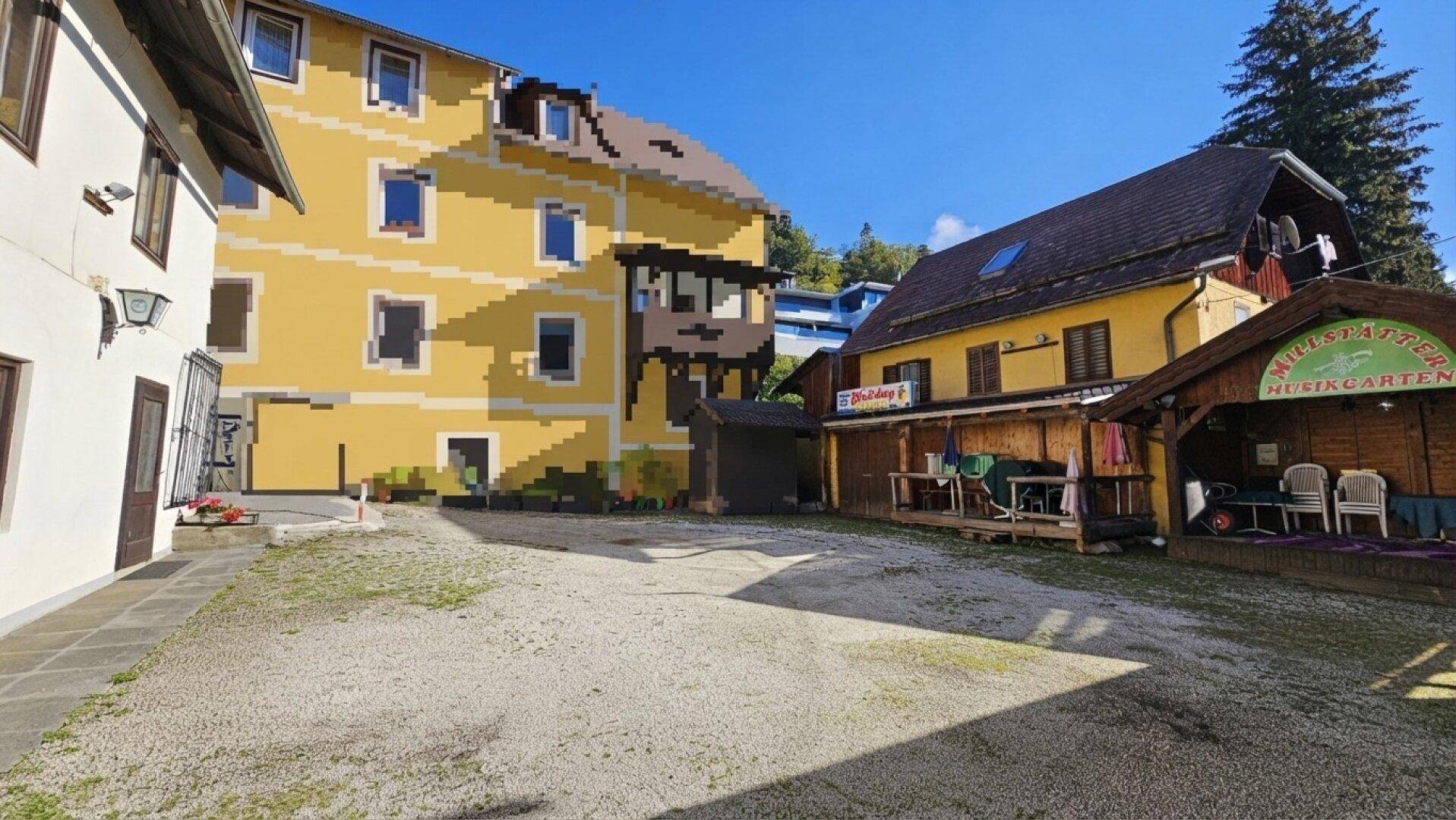 Innenhof mit Kiesfläche, umgeben von Gebäuden, darunter ein gelbes Haus und ein Musikgarten.
