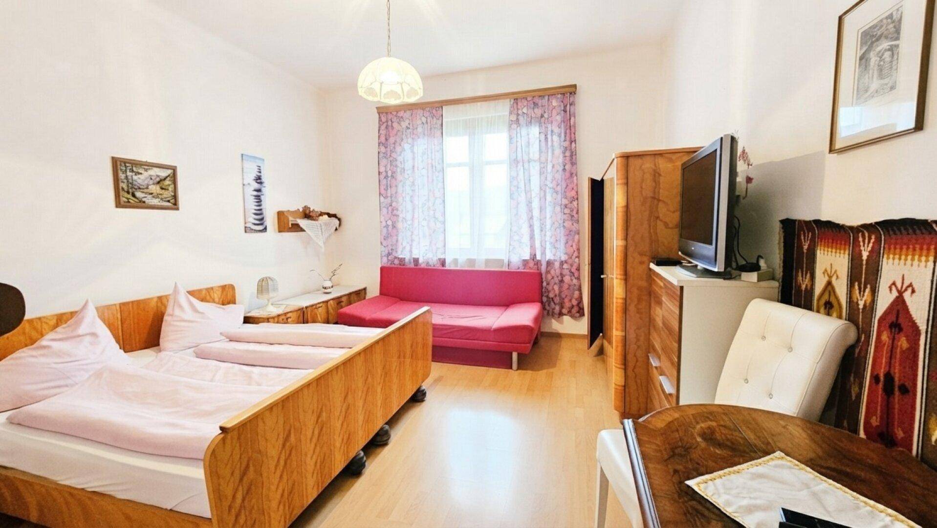 Geräumiges Schlafzimmer mit Doppelbett, Sofa und traditionellen Holzmöbeln unter hellem Licht.