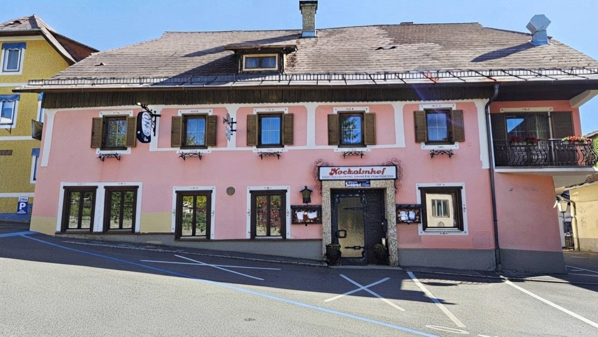 Traditionelles Gebäude mit rosafarbener Fassade, Holzbalkonen und einem Schild des Gasthofs "Hockalminhof".