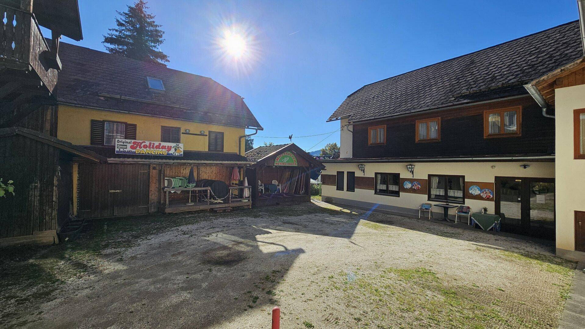 Sonniger Innenhof mit Kiesfläche, umgeben von traditionellen Gebäuden unter strahlend blauem Himmel.