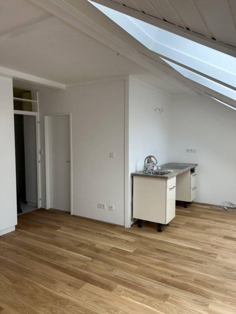 Geräumiger Dachbodenbereich mit Holzboden, Dachschrägen und vorbereiteter Küchennische.