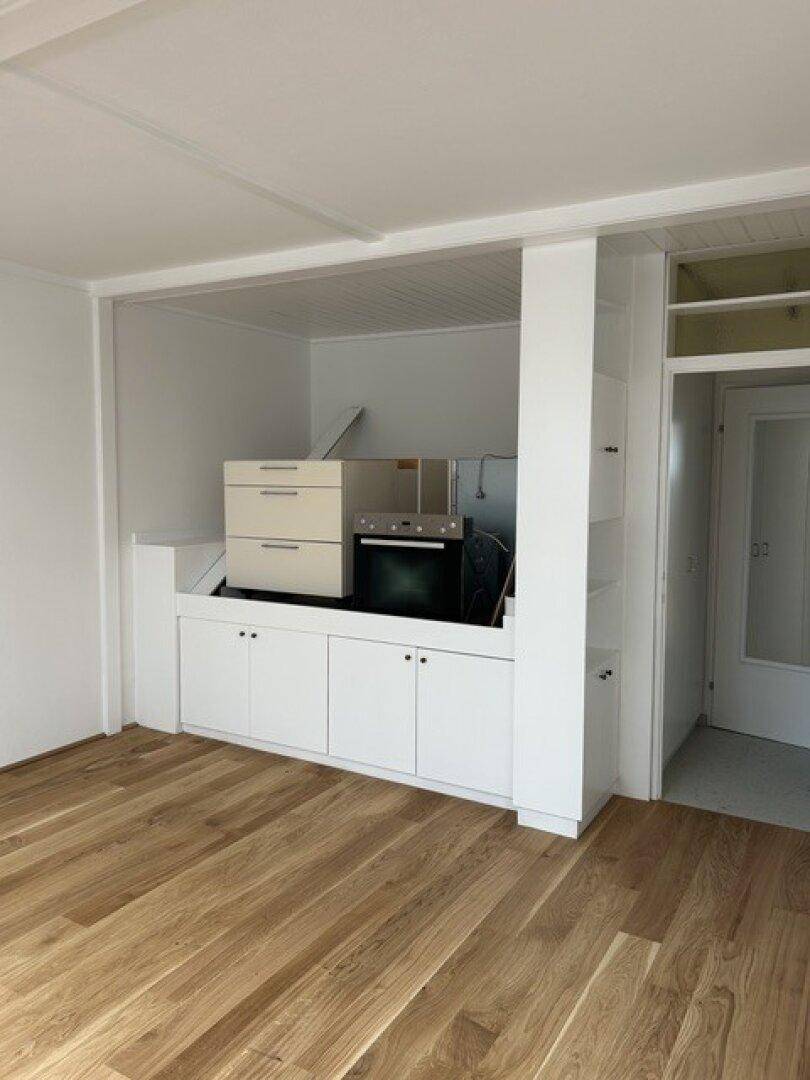 Moderne Küchenzeile mit Einbauschränken, Backofen und Holzdielenboden in hellem Raum.