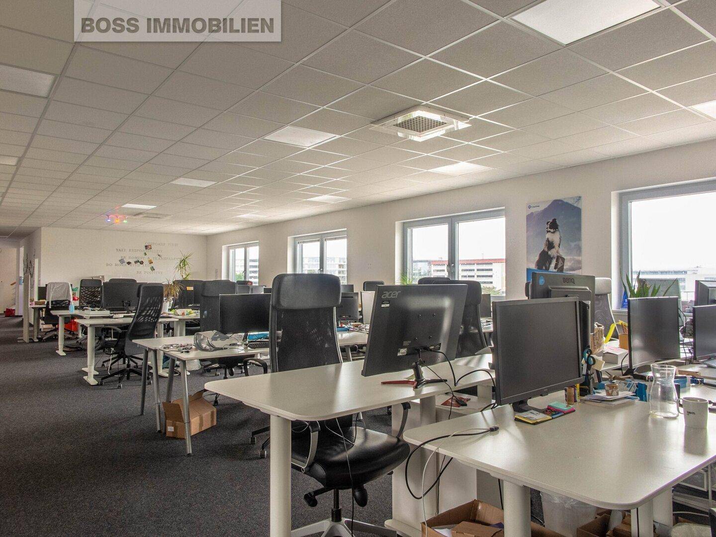 Großes, offenes Büro mit zahlreichen Arbeitsplätzen, modernen Büromöbeln und viel Tageslicht durch die Fenster.