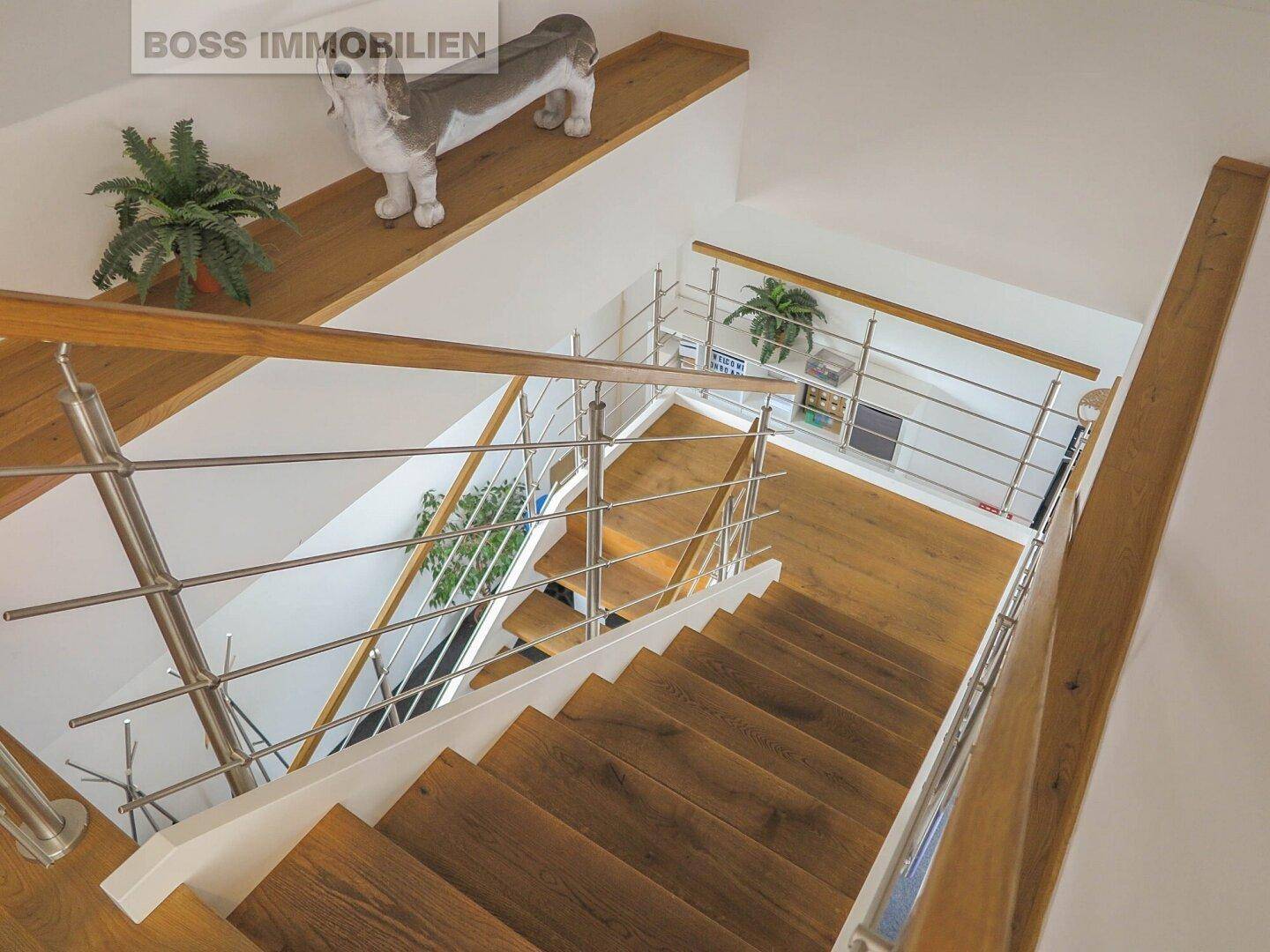 Elegante Holztreppe mit modernen Edelstahlgeländern, die verschiedene Ebenen des Gebäudes stilvoll verbindet.