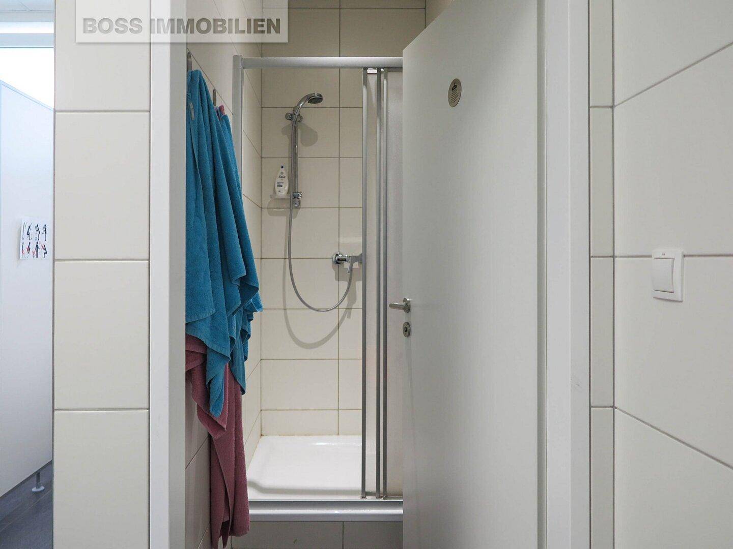Funktionale Dusche mit weißen Fliesen und Glastür in einem modernen Badezimmer, das sehr gepflegt ist.