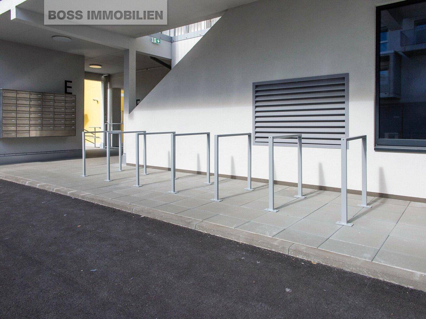 Außenbereich mit Fahrradständern und Briefkästen vor einem modernen Gebäude.