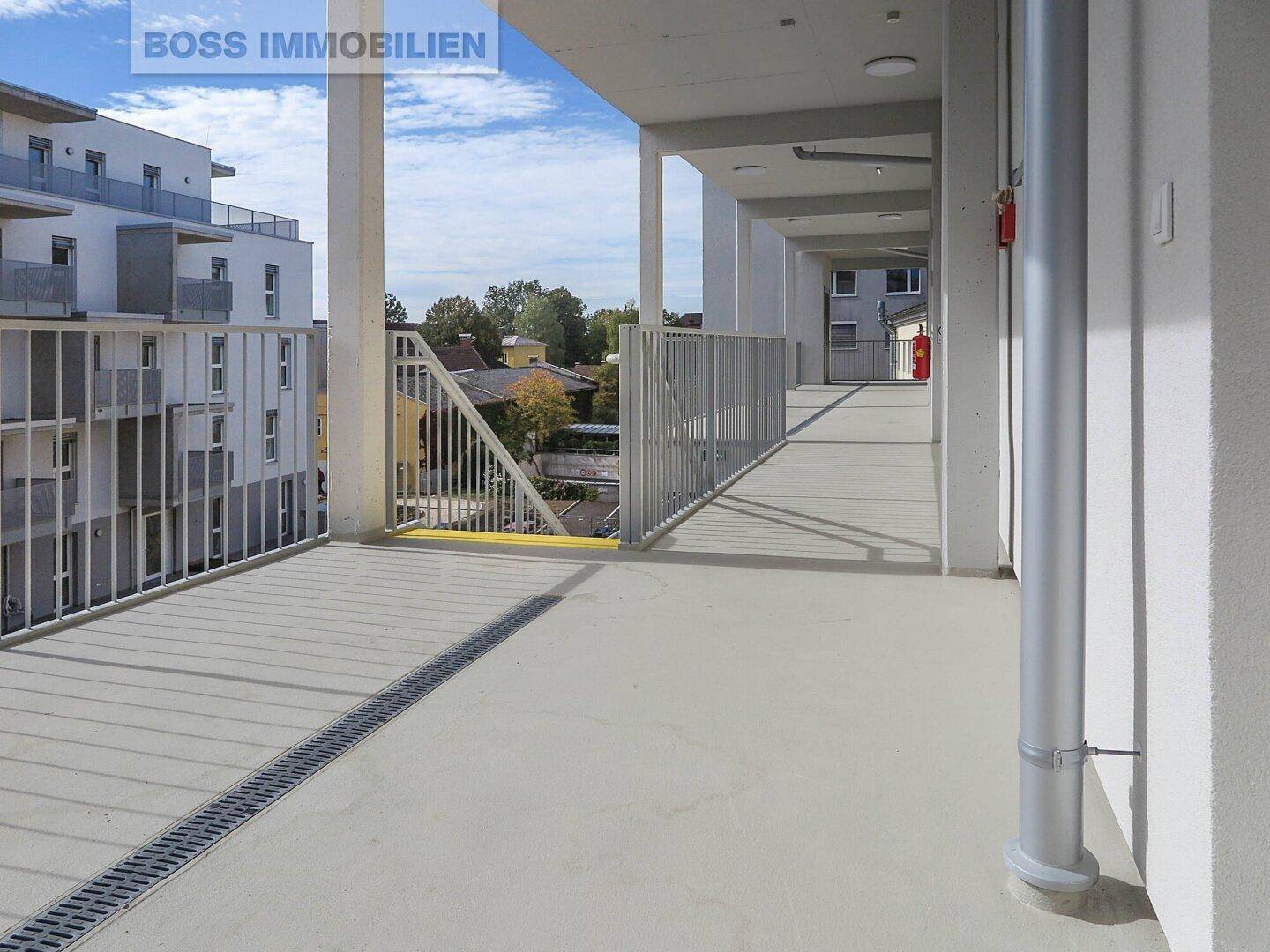 Heller Außenflur oder Balkon mit Betonboden und Metallgeländer, der zu den Wohneinheiten führt.