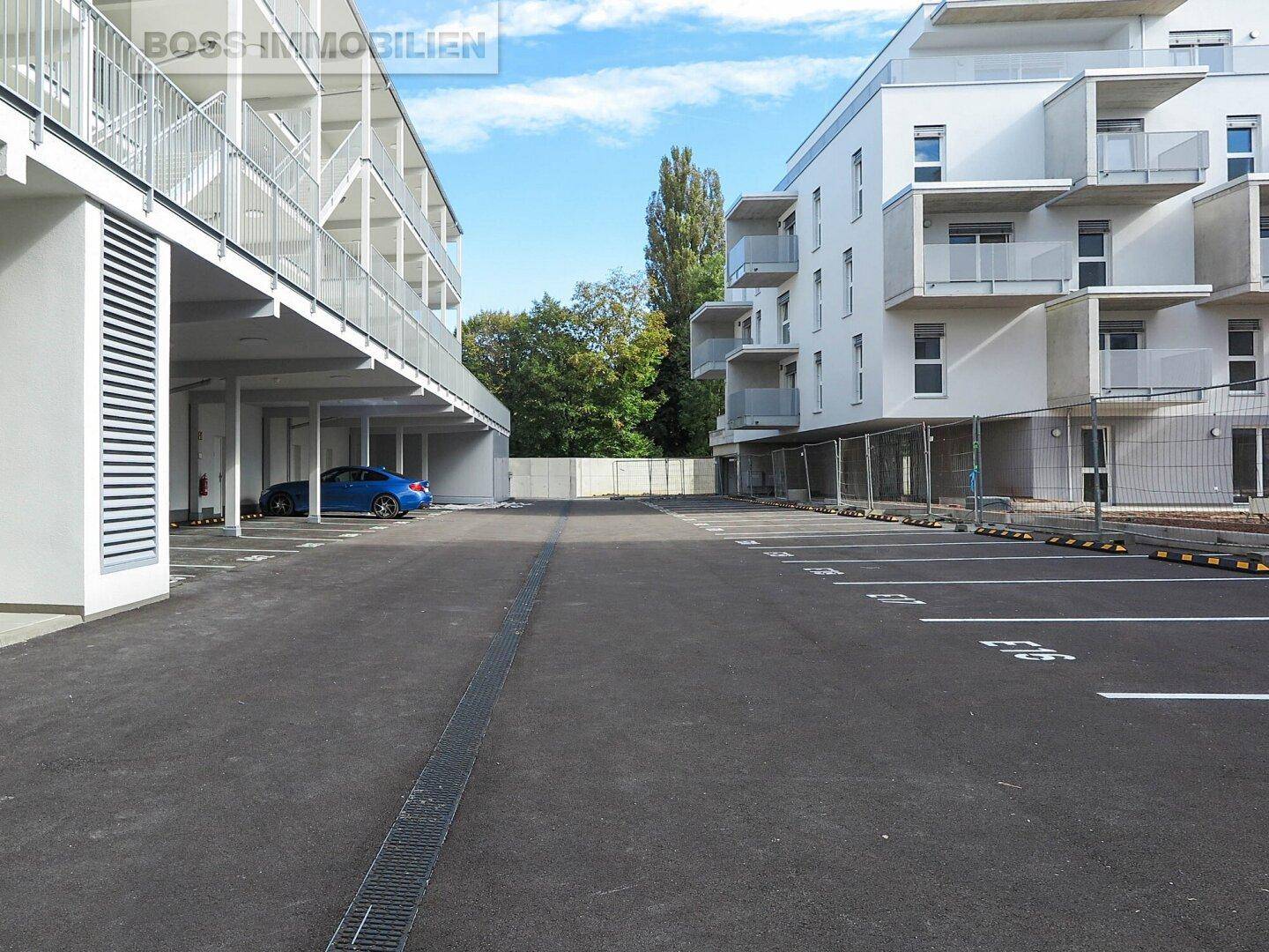 Großer Außenparkplatz mit markierten Stellplätzen zwischen zwei modernen Gebäuden.