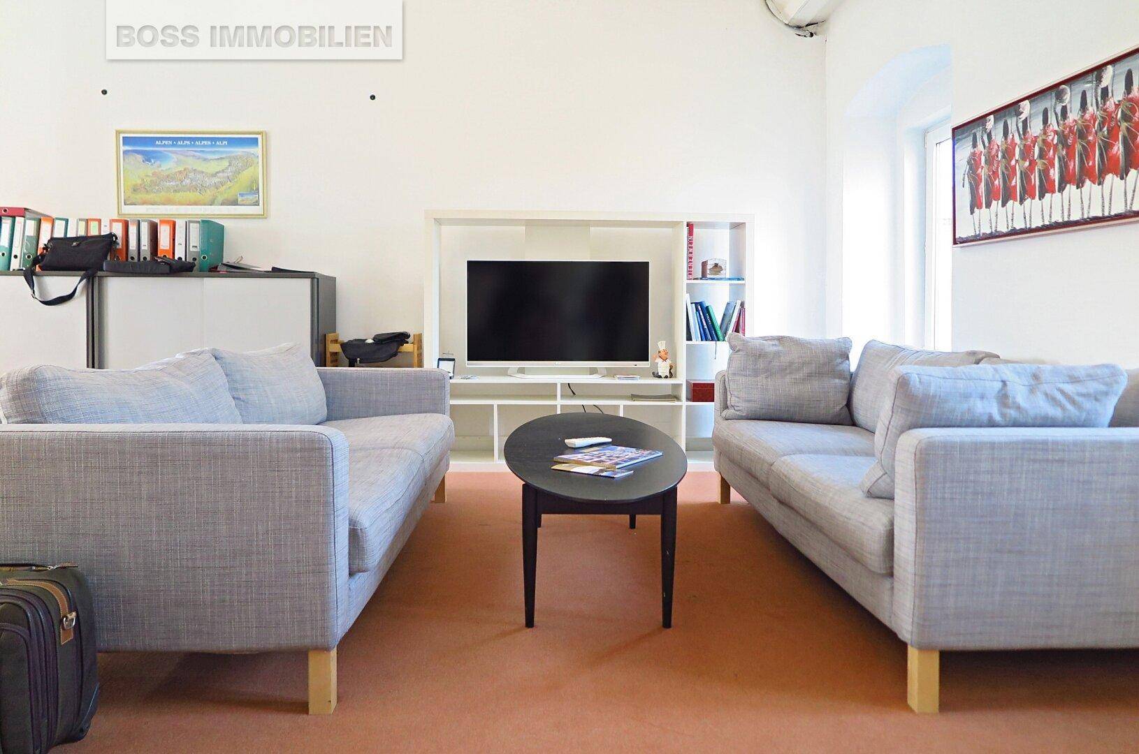 Büroraum mit zwei Sofas, Couchtisch und Fernseher, auf einem orangefarbenen Teppichboden.