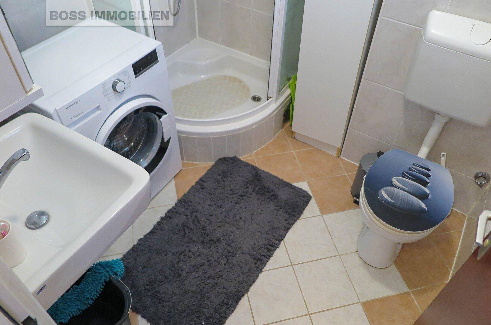 Funktionales Badezimmer mit Duschkabine, Waschmaschine und hellen Fliesen.