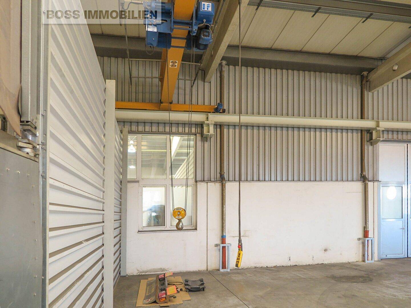 Detailansicht der Lagerhalle mit Krananlage, Wellblechwänden und einem Fenster, das Tageslicht hereinlässt.