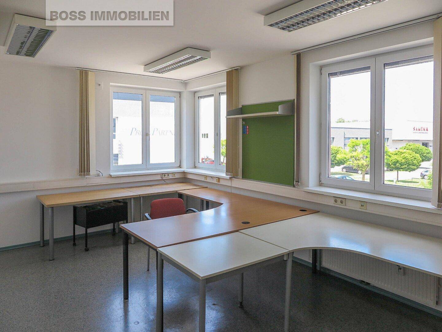 Helles Büro mit mehreren Schreibtischen, großen Fenstern und funktionaler Beleuchtung, bereit zur Einrichtung.