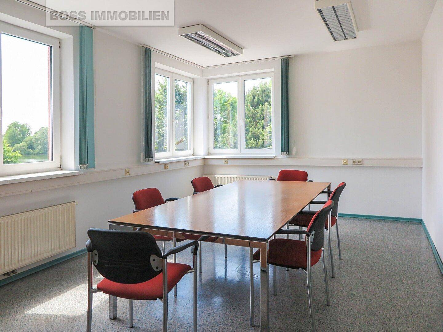 Besprechungsraum mit großem Konferenztisch, bequemen Stühlen und viel Tageslicht durch die Fenster.
