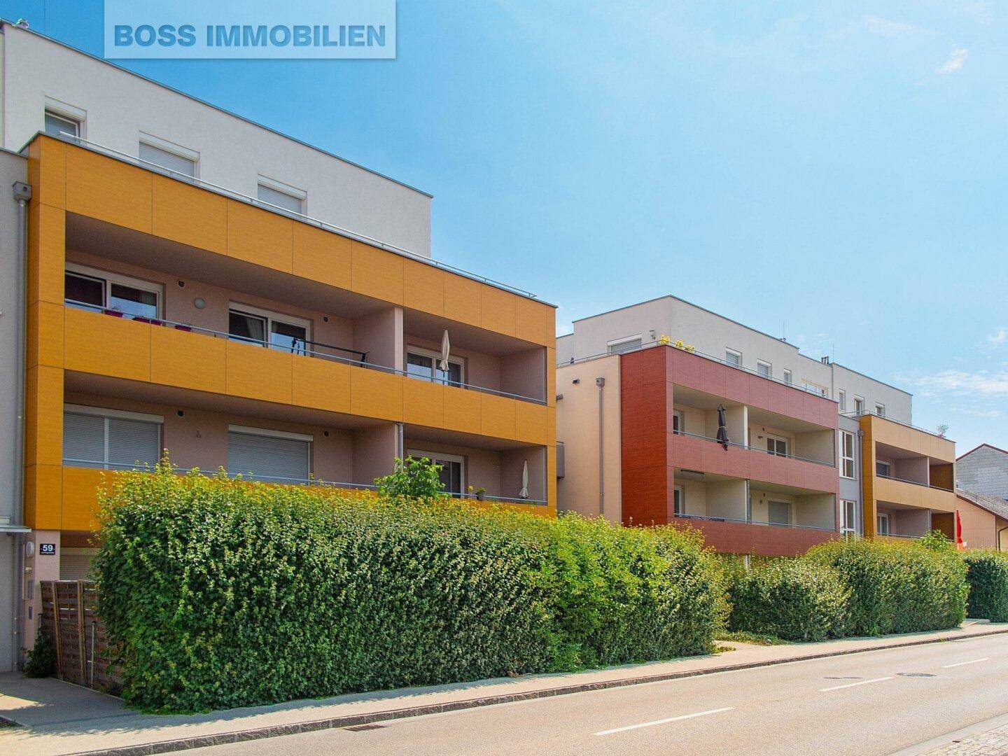 Modernes Mehrfamilienhaus mit farbigen Balkonen und gepflegter Hecke entlang der Straße.