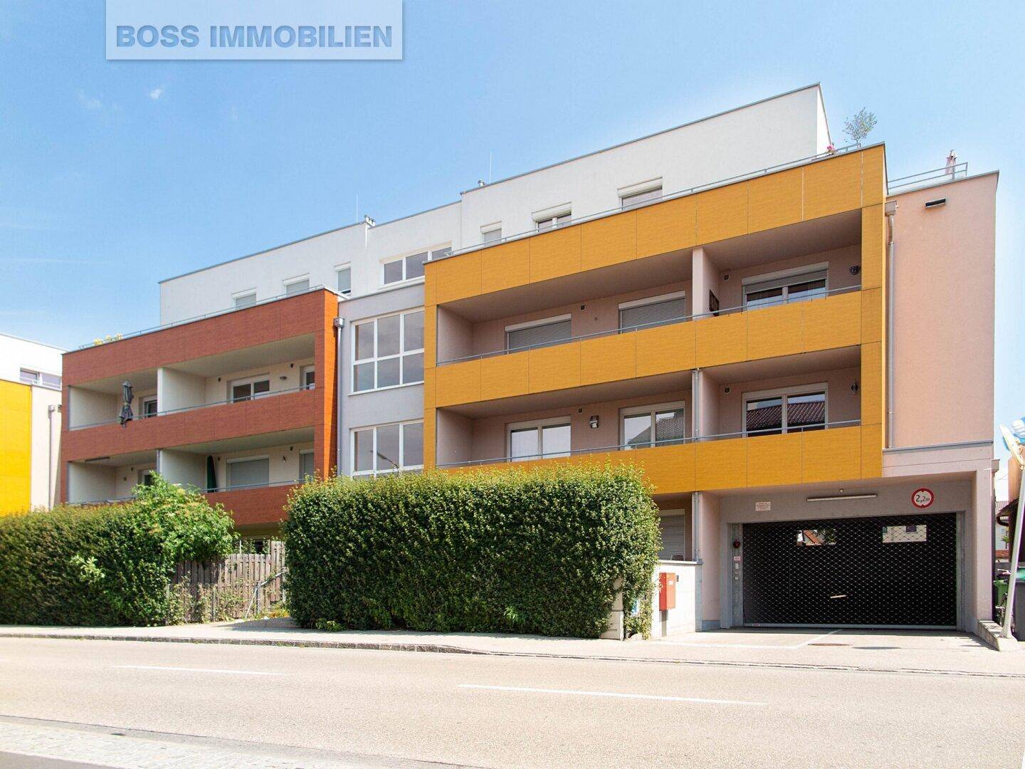 Ansicht des modernen Wohngebäudes mit farbigen Balkonen und Zufahrt zur Tiefgarage.